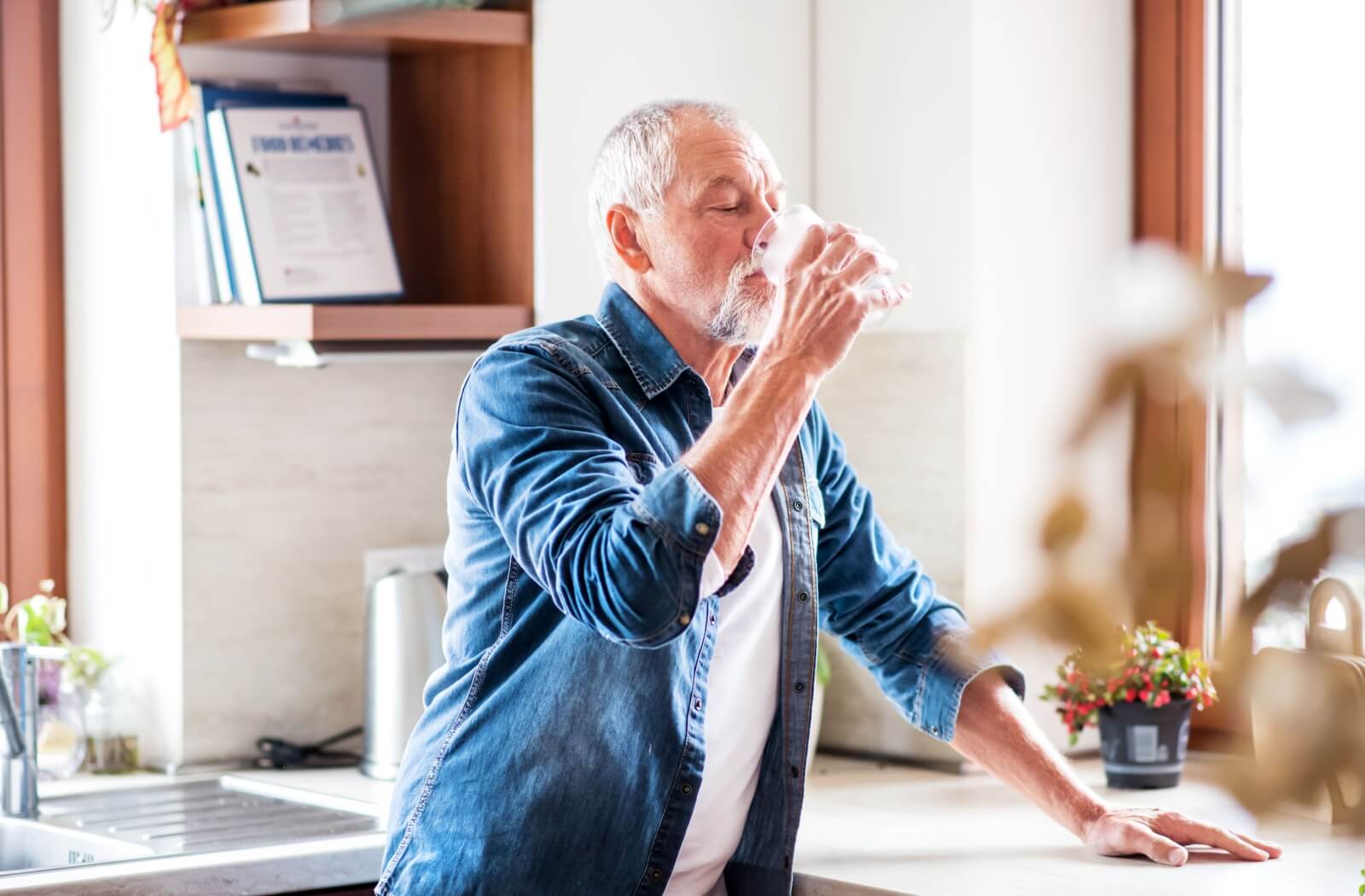 An older adult man drinking water from a glass.