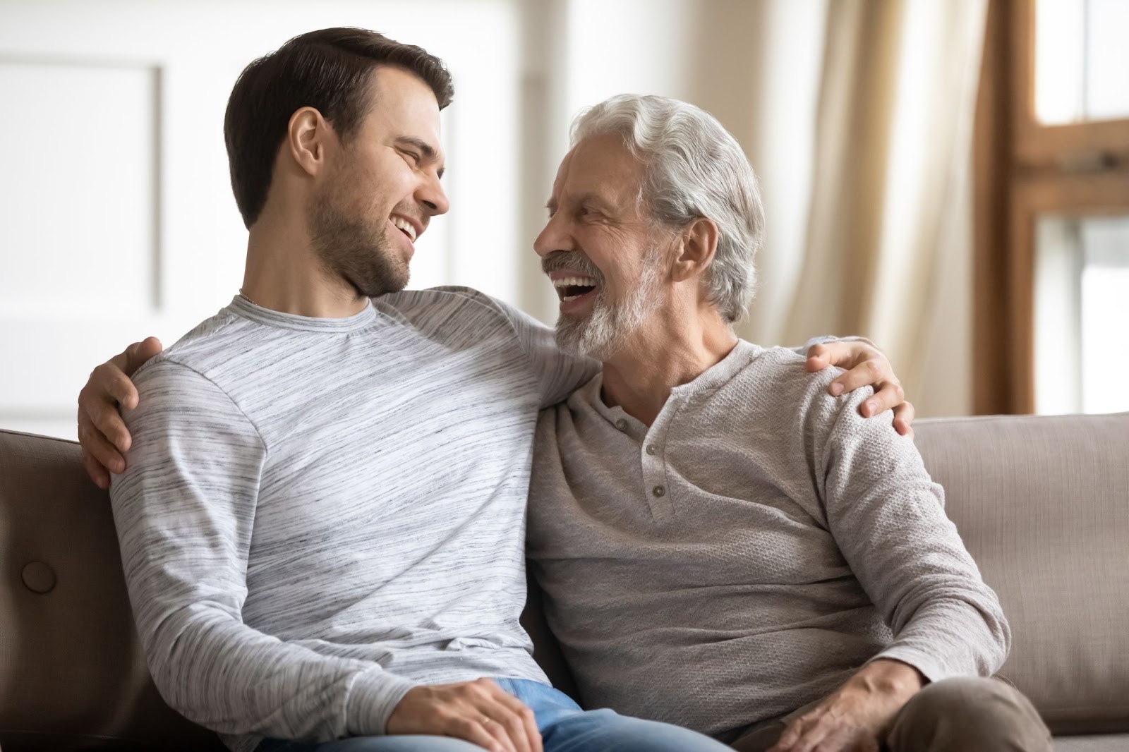 An adult man smiling with his arm around his senior father.