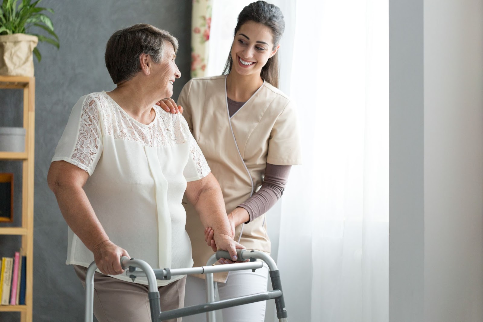 A smiling caregiver helps a senior get around with her walker.