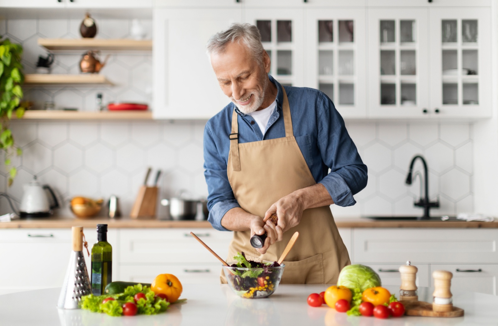 An older adult smiling while grating pepper into a brain-friendly salad in their kitchen.