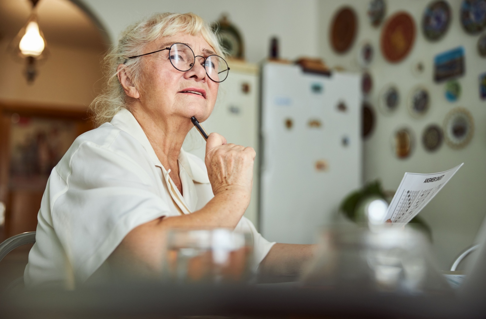 An older adult thinking while writing their answers on a trivia card at home.