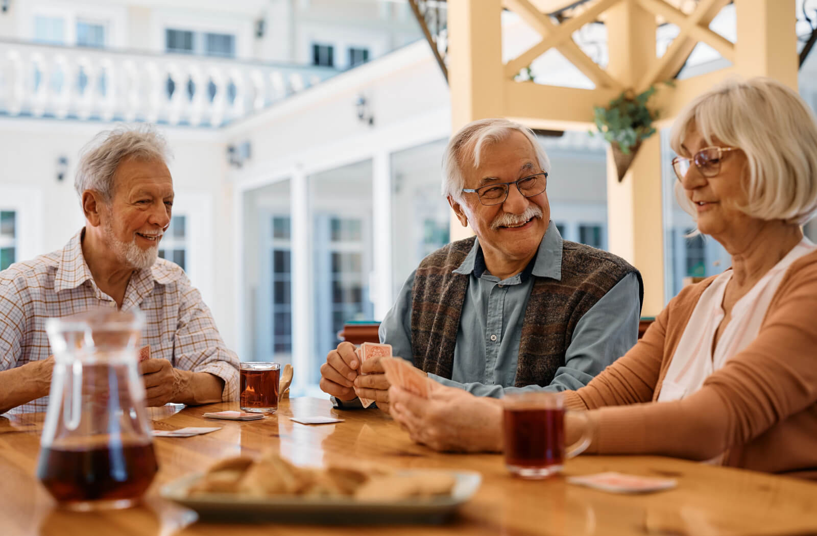 A group of older adults laughing while playing a trivia card game on an outdoor patio.